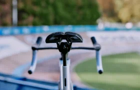 Primer plano de una bicicleta con el sillín y el manillar PRO Stealth 3D, con una pista de velódromo al aire libre difuminada y una exuberante vegetación de fondo.
