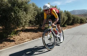 Un ciclista con un maillot rojo y amarillo pedalea en una bicicleta de carretera LOOK 795 Blade RS 3 por una carretera asfaltada cerca de Nevers, bordeada de árboles y bajo un cielo despejado.