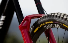 Primer plano de la rueda delantera de una bicicleta de montaña en el que se aprecia el neumático con la inscripción «Emperor» y la llanta «DT Swiss», con parte de una horquilla de suspensión roja a la vista, lo que pone de relieve los neumáticos de MTB de gama alta diseñados para el ciclismo de gravedad.