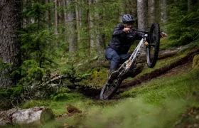 Una persona con casco monta en bicicleta de montaña equipada con neumáticos Pirelli Scorpion MTB por un sendero forestal embarrado, levantando tierra e inclinándose en las curvas entre árboles y vegetación.