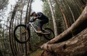 Una persona que lleva casco monta en una bicicleta de montaña equipada con neumáticos Pirelli Scorpion MTB y salta desde un tronco caído en un bosque frondoso; la imagen está tomada desde un ángulo bajo.