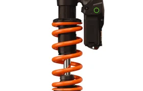 Primer plano de un amortiguador negro y naranja de bicicleta o motocicleta, con un componente electrónico acoplado, que muestra ingeniería con el factor X.