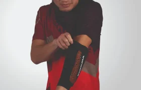 Una persona que viste un traje deportivo rojo y negro se ajusta la manga del brazo Endura.