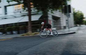 Un ciclista, con casco y equipación de ciclismo, recorre a gran velocidad una esquina de una calle de Nevers montado en una bicicleta de carretera LOOK 795 Blade RS 3, con un efecto de desenfoque de movimiento en el fondo.