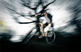 Una persona conduce una Fantic Sierra e-MTB a toda velocidad por un bosque, con el motor Bosch CX Gen5 impulsándola mientras el fondo se difumina en un efecto dinámico de movimiento radial.