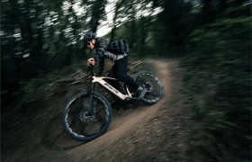 Una persona con casco conduce rápidamente una Fantic Sierra e-MTB por un sendero de tierra en una zona boscosa, rodeada de árboles y vegetación.