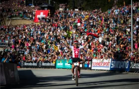 Un ciclista ataviado con un maillot suizo celebra su llegada a la meta en primer lugar, con los brazos en alto, ante una multitud que le aclama en una prueba ciclista en honor de la retirada del legendario Nino Schurter.