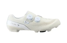 Vista lateral de unas zapatillas de ciclismo blancas Shimano RX710 con dos mandos BOA y detalles perforados, con la inscripción «RX7» cerca del talón, diseñadas con tecnología de competición para un rendimiento óptimo en grava.