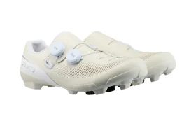 Un par de zapatillas de ciclismo Shimano de color blanco roto con parte superior perforada, dos cierres de dial blancos y suelas de goma texturizadas diseñadas para ofrecer agarre en senderos de grava, que incorporan tecnología de competición para un rendimiento óptimo.