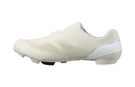 Vista lateral de una zapatilla de ciclismo blanca de perfil bajo, con parte superior perforada y suela moldeada, diseñada para pedales automáticos, que incorpora tecnología de competición ideal tanto para el ciclismo en carretera como en grava.