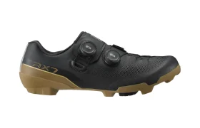 Unas zapatillas de ciclismo negras con suela marrón, dos mandos BOA, parte superior perforada y el logotipo «RX7» en el lateral, representadas de perfil sobre un fondo blanco: estas zapatillas Gravel Shimano RX710 destacan por su tecnología de competición para los ciclistas más exigentes.