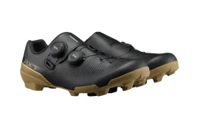 Un par de zapatillas de ciclismo Shimano RX710 negras con suela de goma de color beige, que cuentan con dos cierres de dial en cada zapatilla para un ajuste personalizable; diseñadas especialmente para salidas por grava y mejoradas con tecnología de competición para un rendimiento superior.