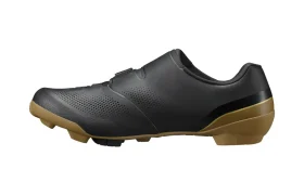 Zapatilla de ciclismo negra con parte superior perforada, cierre de velcro y suela marrón con dibujo, mostrada de perfil sobre un fondo blanco: ideal para salidas de gravel e inspirada en la tecnología de competición de las zapatillas Shimano.