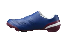 Vista lateral de unas zapatillas de ciclismo Shimano RX710 azules con detalles en granate y perforaciones, que incorporan tecnología de competición para un rendimiento óptimo sobre grava, mostradas sobre un fondo blanco.