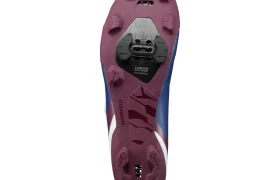 La suela de una zapatilla de ciclismo Shimano RX710, con un dibujo morado, una cala Shimano SPD y una placa de compuesto de carbono, vista desde abajo: diseñada a la perfección para salidas por grava e incorporando tecnología de competición.