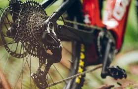 Primer plano del desviador trasero y los engranajes de una bicicleta de montaña, que muestra el SRAM Eagle 90 con un cuadro rojo y radios negros en un entorno al aire libre.