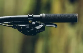 Primer plano de un manillar de bicicleta de montaña con cambio SRAM Eagle y empuñadura de goma texturizada, sobre un fondo natural difuminado. Perfecto para ciclistas que buscan precisión con cambios mecánicos.