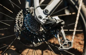 Primer plano de un desviador trasero SRAM Eagle 70 y un cassette de cambios bajo la luz del sol, resaltando los componentes mecánicos y la reluciente cadena de metal.