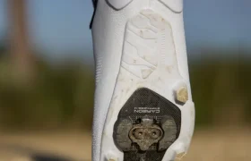 Primer plano de la suela de una Zapatillas Shimano RX910 blanca de ciclismo con una cala SPD negra y suciedad de gravilla en la banda de rodadura, fotografiada al aire libre en un camino escarpado.