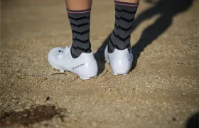 Persona con RX910 S-Phyre Zapatillas Shimano y calcetines con estampado de chevrones negros y grises de pie en un camino de grava.