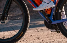 Primer plano del pie de un ciclista con una zapatilla blanca sobre un pedal LOOK, con neumáticos Continental y un camino de grava, perfecto para explorar el ecosistema de pedales Gravel.