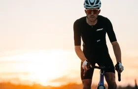 Un ciclista con ropa negra, casco y gafas de sol monta en una bicicleta LOOK con pedales Gravel al atardecer, abrazando el ecosistema de pedales al aire libre.