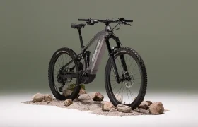 Una Fantic Sierra e-MTB gris mate, propulsada por el motor Bosch CX Gen5, se muestra sobre grava y rocas sobre un fondo verde apagado.