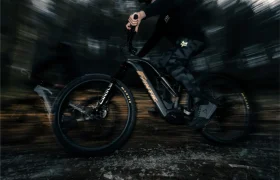 El ciclista atraviesa a toda velocidad un sendero boscoso en una Fantic Sierra e-MTB con suspensión integral, el desenfoque de movimiento resalta el movimiento y el potente motor Bosch CX Gen5 en un entorno oscuro y dinámico.