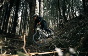 Una persona con casco conduce una Fantic Sierra e-MTB con motor Bosch CX Gen5 por una pista forestal rodeada de árboles y follaje.