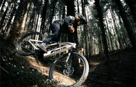 Una persona conduce una Fantic Sierra e-MTB por un sendero de tierra a través de un denso bosque, inclinándose bruscamente mientras toma una curva, propulsada por el motor Bosch CX Gen5.