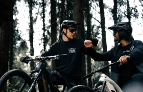 Dos ciclistas con casco y gafas de sol se chocan los puños con sus bicicletas eléctricas Bosch CX Gen5 en un bosque soleado.