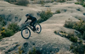 Una persona que lleva casco conduce una bicicleta de montaña UNNO MITH por un terreno accidentado y rocoso con escasa vegetación.