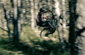 Una persona realiza con confianza un caballito en su bicicleta de montaña UNNO MITH, maniobrando con gracia a través del bosque mientras los árboles se difuminan en un fondo lleno de movimiento.