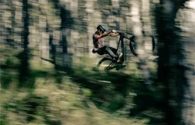 Una persona que lleva un casco realiza un salto en una bicicleta de montaña UNNO MITH en un bosque, con el desenfoque de movimiento capturando la velocidad.