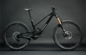 La UNNO MITH, una elegante bicicleta de montaña negra con un cuadro de suspensión total, frenos de disco y neumáticos con tacos, está ingeniosamente ubicada sobre un fondo gris oscuro.