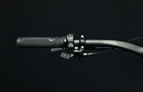 Primer plano de un manillar de bicicleta UNNO MITH que muestra empuñaduras texturizadas y elegantes palancas de cambio sobre un fondo negro.