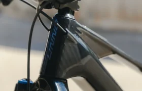 Primer plano del tubo de dirección y el manillar de una bicicleta negra, que muestra el logotipo UNNO MITH con detalles en azul y blanco en el cuadro.