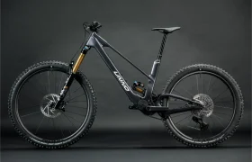 La bicicleta de montaña negra UNNO MITH cuenta con horquillas de suspensión grandes, neumáticos anchos y un cuadro elegante, resaltado sobre un fondo oscuro y liso.