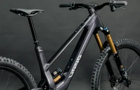 La bicicleta de montaña eléctrica UNNO MITH cuenta con un elegante cuadro negro, neumáticos anchos y doble suspensión, todo ello elegantemente presentado sobre un fondo oscuro y liso.
