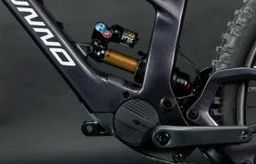 Primer plano de un elegante cuadro de bicicleta eléctrica UNNO MITH negro con un sistema de suspensión FOX y un motor eléctrico integrado, con marca y cables visibles sobre un fondo oscuro.