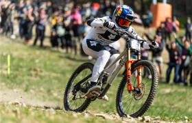 Un ciclista de montaña, vestido con un maillot de competición blanco y negro, desciende a toda velocidad por un sendero rocoso ante una multitud de espectadores, demostrando la precisión del TRP EVO PRO Anniversary Edition en este evento de edición limitada celebrado en la Península Ibérica.