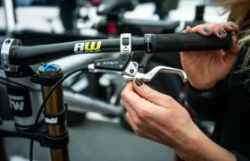 Una persona ajusta la palanca de freno TRP EVO PRO Anniversary Edition en el manillar de una bicicleta de montaña con el logotipo de RW, sujetando la palanca con una mano y utilizando una herramienta con la otra; se trata de una edición limitada exclusiva disponible en la Península Ibérica.