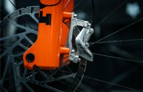 Primer plano de una pinza y un disco de freno delantero TRP EVO PRO Anniversary Edition en una horquilla naranja, en el que se ven los radios y parte de la rueda; esta edición limitada se inspiró en los recorridos por la Península Ibérica.