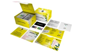 Un estuche de la marca, de color amarillo y blanco, con varios folletos plegados, tarjetas y material impreso esparcidos por dentro, en los que aparecen los logotipos del Tour de Francia y de Škoda.