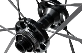 Primer plano del buje de una rueda de bicicleta con radios metálicos que se extienden radialmente hacia fuera, en el que se aprecian con detalle las piezas mecánicas y el logotipo «Shimano Dura-Ace WH-R9370» en el buje central, lo que pone de relieve la ingeniería de precisión que suele caracterizar a las ruedas de carbono.