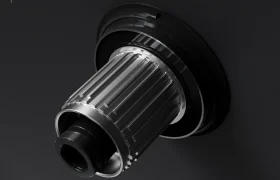 Primer plano de un componente metálico del buje de una bicicleta montado sobre una superficie negra, con ranuras y salientes para su fijación; compatible con las ruedas WH-R9370 Ruedas Shimano Dura-Ace y diseñado para admitir radios de carbono de última generación.