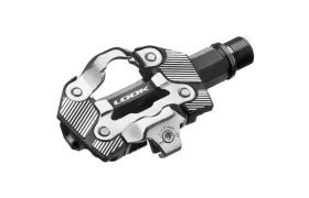 Un pedal LOOK negro y plateado, diseñado para el ecosistema de pedales de grava, lleva el nombre de la marca en el centro y se muestra sobre un fondo blanco.
