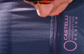 Primer plano de un ciclista que lleva casco y un maillot oscuro Castelli Corretto LS, un modelo de manga larga con el emblemático logotipo rosa y la inscripción «Performance Innovation Design».