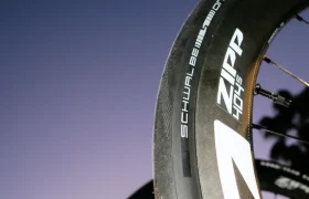 Primer plano de una rueda de bicicleta Zipp 404 S con un neumático Schwalbe One, con un cielo morado claro de fondo, que destaca su velocidad y su calidad superior a un precio impresionante.