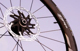 Primer plano de una rueda de bicicleta Zipp 404 S con radios negros, un disco de freno y una llanta con el logotipo de la marca, con un cielo de color morado pálido de fondo; diseñada para la velocidad y el rendimiento.